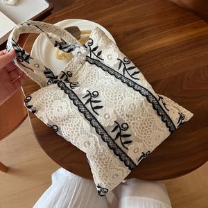 Detail of white lace tote bag featuring intricate black floral embroidery and retro design