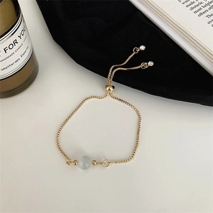 Détail d'un bracelet doré réglable avec perle d'opale sur fond blanc élégant