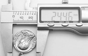 Detail shot measuring a vintage 24.46 mm stainless steel Greek coin pendant with caliper