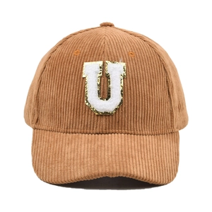 Detail der braunen Cord-Baseballkappe mit weißem U-Aufnäher und goldenen Pailletten