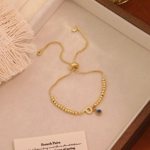 Dettaglio di un bracciale dorato regolabile con lettera P e ciondolo occhio blu