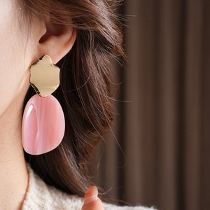 Gros plan de boucles d'oreilles ovales en acrylique rose avec clous dorés sur un mannequin
