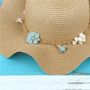 Détail du chapeau de paille orné de fleurs bleues et beige avec des pompons colorés