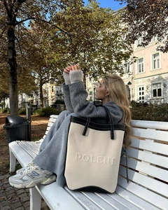 Detailed view of the Polene brand logo embossed on a cream canvas tote bag with black leather