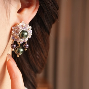 Close-up of vintage floral earrings with purple petals and green pearl tassels on model