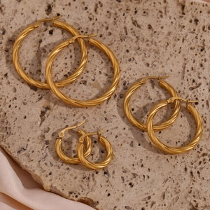 Detailed view of three pairs of twisted gold hoop earrings on a textured stone display
