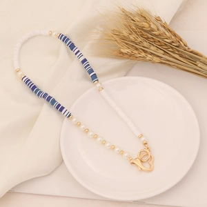Bohemian clay bead necklace with gold heart clasp on a stylish white plate