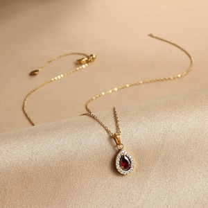 Detail of water drop zircon pendant with red gemstone on golden chain on satin