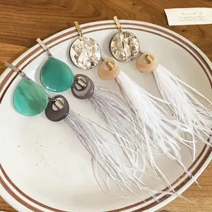 Boucles d'oreilles bohèmes à pompons de plumes et perles en résine sur une assiette en céramique