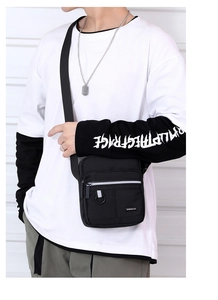Detail of black oxford fabric crossbody bag showing zippers and reflective strip on a model