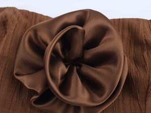 Detailed close-up of a 3D satin flower appliqué on brown pleated fabric