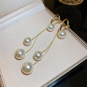 Détail de boucles d'oreilles à pompons dorés avec trois perles graduées dans un écrin