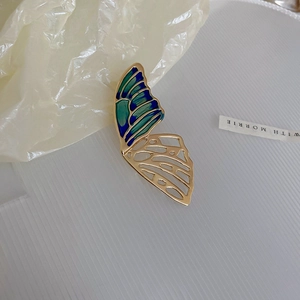 Detail of butterfly brooch featuring blue enamel wings and golden hollow metalwork