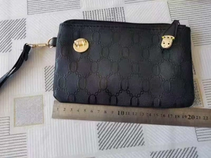 Detail of black synthetic leather pouch with embossed letter pattern and gold zipper