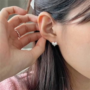 Close-up of a model wearing heart-shaped silver earrings and a twisted metal ring