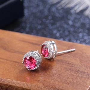 Macro detail of silver halo stud earrings featuring a round red zircon and tiny white stones