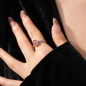 Close-up of a silver ring with a red oval gemstone on a model's hand with black velvet
