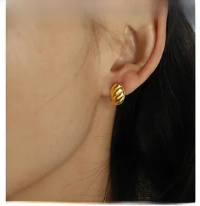 Close-up of gold C-shaped earring with spiral texture on female model's ear