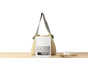 Detail of beige paper rope woven bag with black and white striped canvas shoulder strap