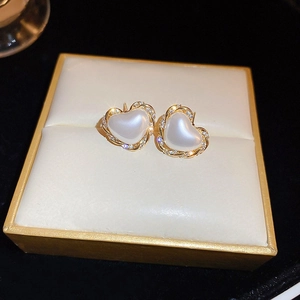 Macro shot of gold plated heart-shaped pearl earrings with sparkling rhinestones and twisted texture