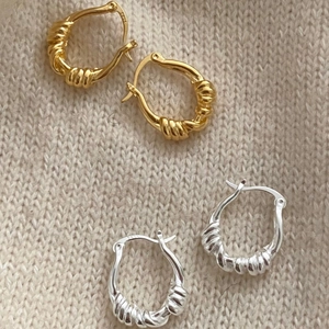 Close-up of gold and silver S925 sterling silver twisted rope hoop earrings on knit fabric