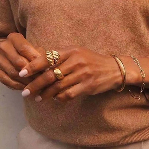 Detail of twisted croissant ring and smooth golden band worn on model's hand
