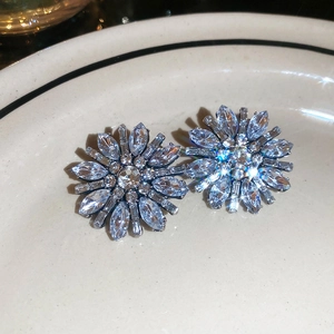 Close-up of light blue flower stud earrings with marquise crystals on a ceramic tray