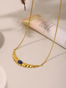 Detail of a crescent moon gold necklace with hammered metal texture and a blue lapis stone