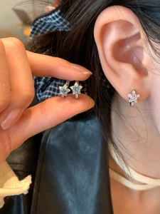 Détails de boucles d'oreilles étoile avec zircon bleu portées à l'oreille et en main