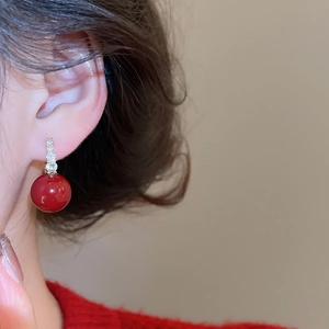 Close-up of red zircon earrings on model, featuring a round bead and gold metal finish