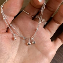 Close-up of double-layer silver bracelet featuring small beads and a 3D heart charm
