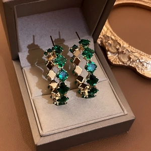 Macro shot of gold hoop earrings with emerald square-cut gemstones in a jewelry box