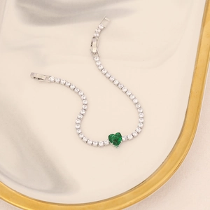 Macro detail of silver bracelet featuring a green heart stone and white cubic zirconia