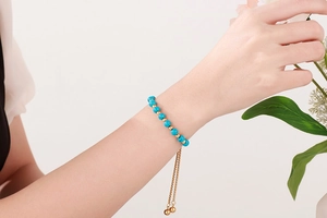 Bracelet ajustable doré avec perles turquoise porté par un mannequin au poignet