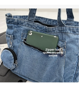 Detail of blue denim tote bag showing front zipper pocket with a tablet and round coin purse