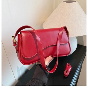 Detail shot of bright red leather shoulder bag held by hand to show size and scale