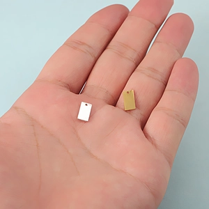 Macro view of gold and silver rectangle pendant charms held in hand for size reference
