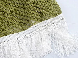 Macro shot of olive green mesh knit fabric with white fringe details on the dress hem