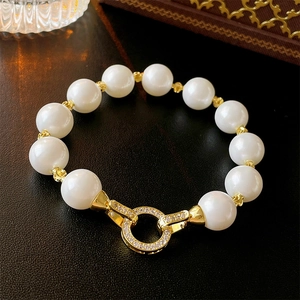 Detail of elegant pearl bracelet with gold zircon paved clasp on leather surface