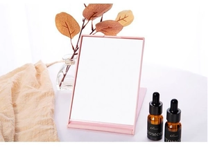 Pink folding makeup mirror on a white table with minimalist lifestyle decor and prop bottles