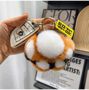 Plush animal paw keychain with orange and white fur and lucky charm hanging on a bag