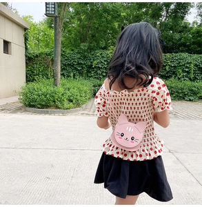 Pink cat-shaped kids crossbody bag in PU leather worn by a child in an outdoor park