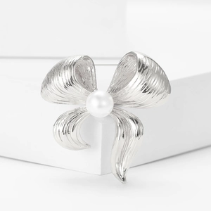 Detailed close-up of a silver bow brooch with a central white pearl and brushed metal texture