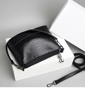 Detail of black crossbody bag featuring crocodile texture and dual zipper compartments