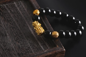 Close-up of golden Pixiu charm and black obsidian-like beads on a dark wooden tray