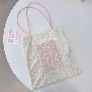 Detail of a white lace tote bag featuring pink vintage patchwork and rope handles