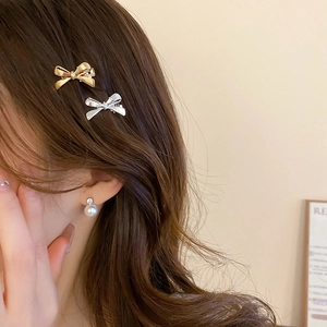Close-up of golden and silver bow hair clips with a pearl earring worn by a model