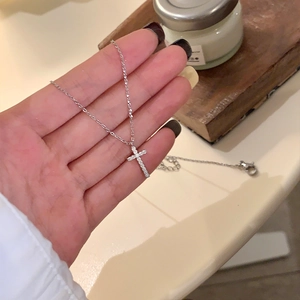 Detailed close-up of a silver cross necklace with moissanite stones held by a person
