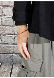 Gros plan d'un bracelet gourmette doré en acier inoxydable porté dans un style streetwear