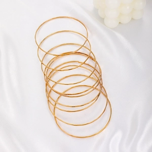 Detailed view of layered minimalist gold bracelets on soft white silk fabric background